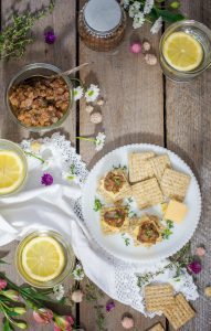 TRISCUIT Crackers topped with Gouda cheese and ploughmans pickle, and glasses with lemon water, overhead shot