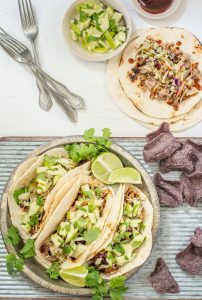 Plate of BBQ shredded pork tacos with blue corn tortilla chips on galvanized placemat.