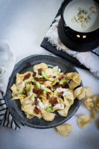 A plate of kettle chips with bacon, green onions and blue cheese fondue